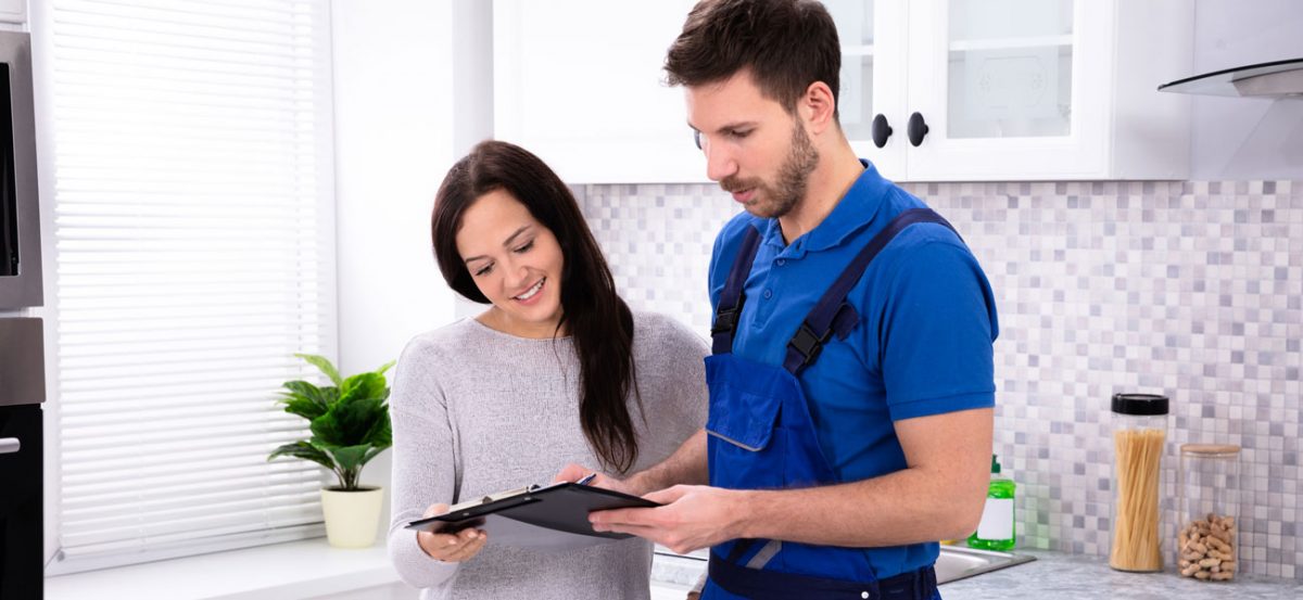 Close-up Of Young Male Plumber Showing Invoice To Woman In Kitchen